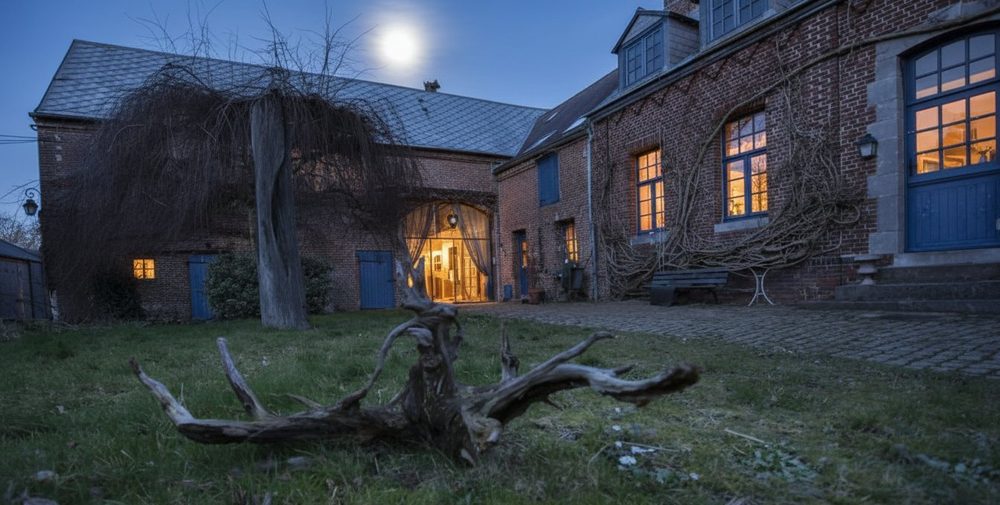 Les Granges de Béthencourt at nightfall. Lit windows, full moon above the roof.